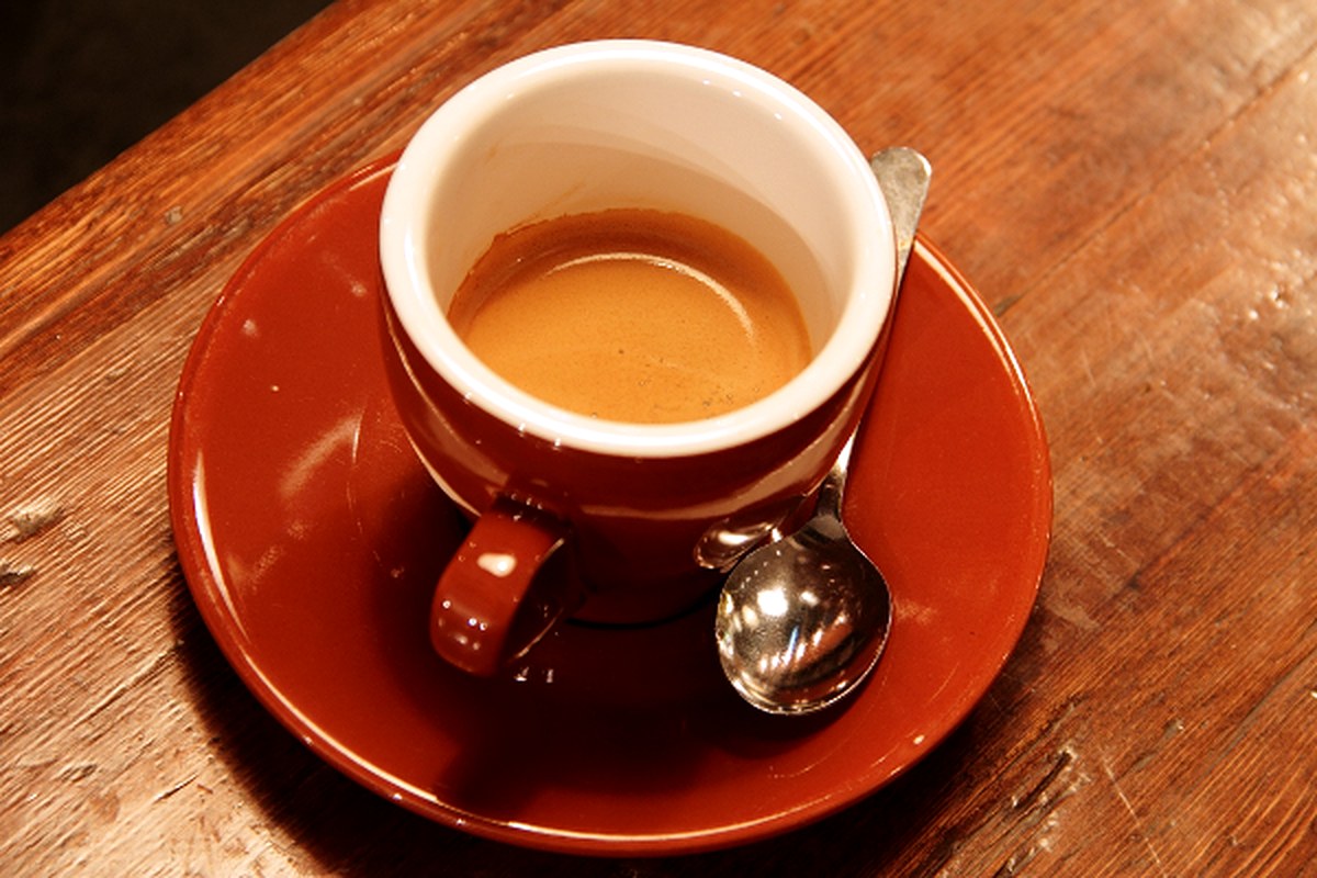 A red cup of coffee and a spoon on a warm wooden tabletop.