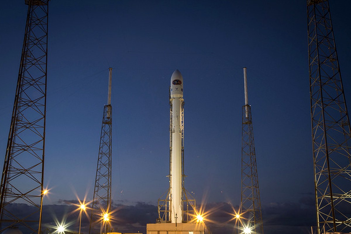 A rocket standing on a launch pad against a deep blue evening sky.